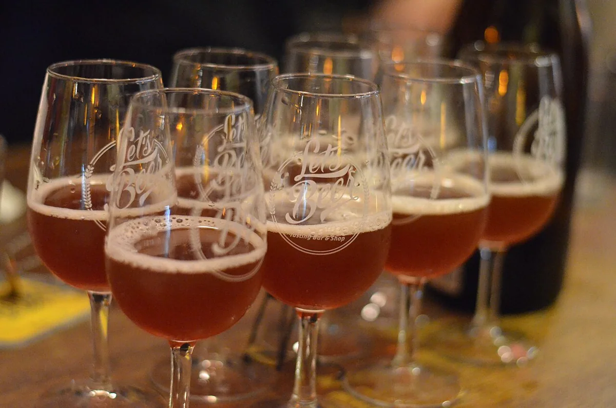 A row of stemmed tasting glasses filled with amber beer on a wooden table.