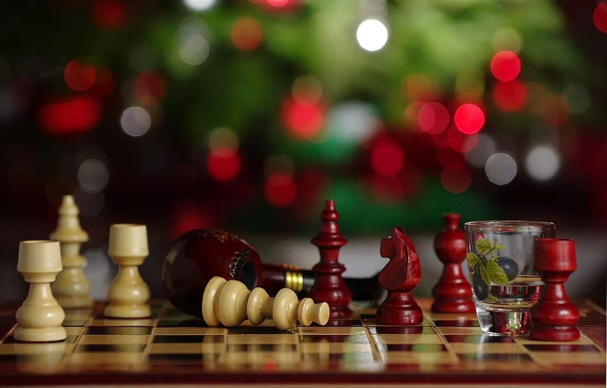 White and dark wooden chess pieces on a chessboard, with softly blurred lights behind them.