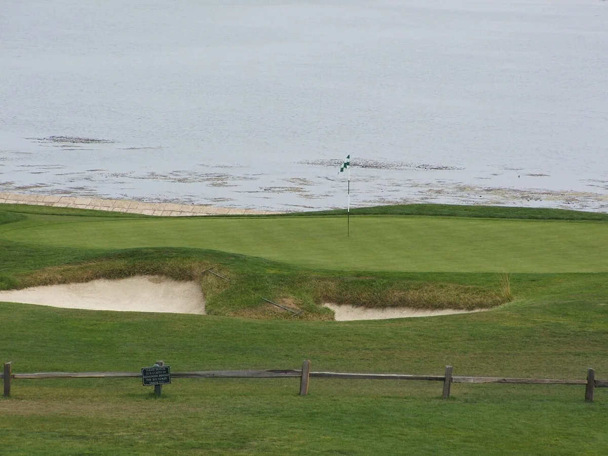 A flag on the 18th green at Pebble Beach, with sand bunkers and the ocean behind it.