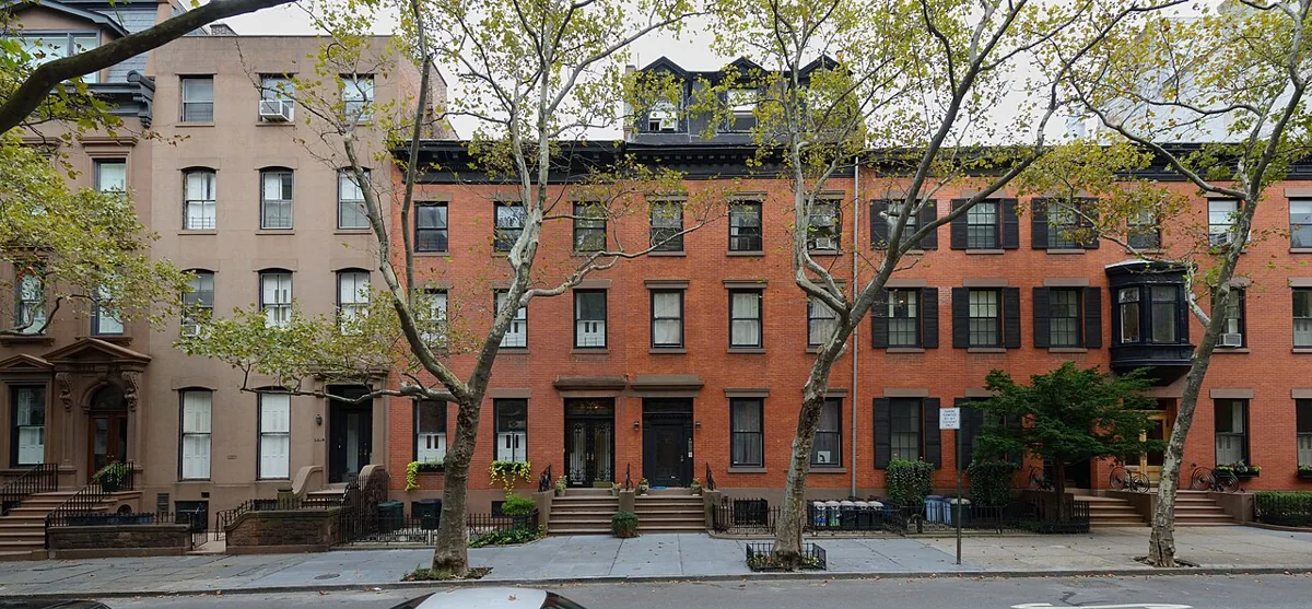 A row of historic brick and brownstone townhouses with front steps and street trees in Brooklyn Heights.